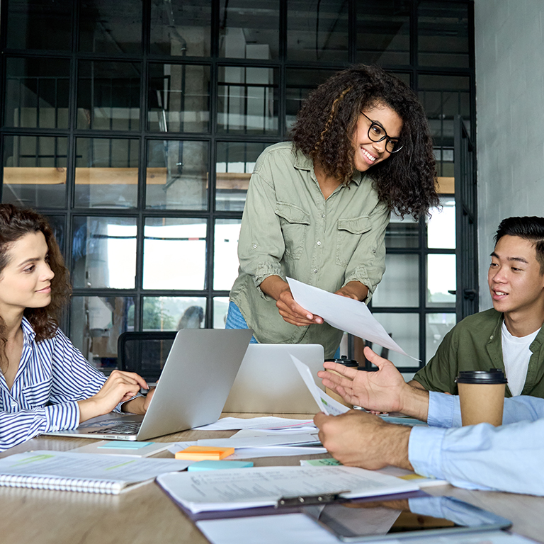 Diverse multiracial young happy cheerful coworkers business startup creative team people students discussing project results with African american mentor leader in contemporary office using laptops.