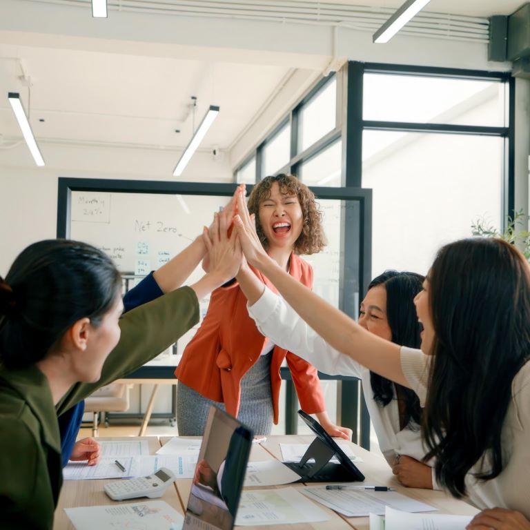 A diverse team of business professionals celebrating with a high-five during an ESG