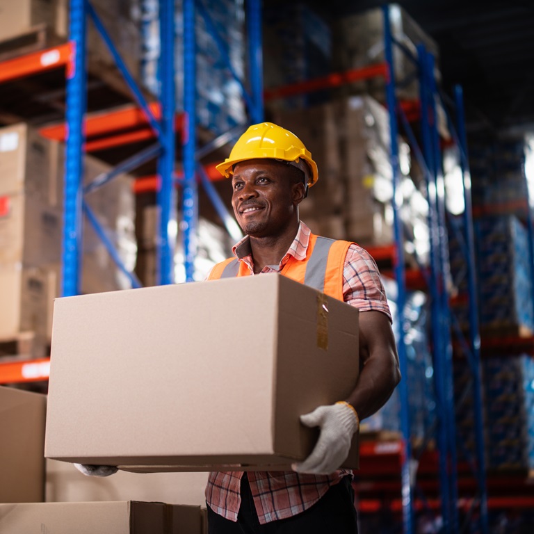 Warehouse worker with safety equipment carrying a big box.