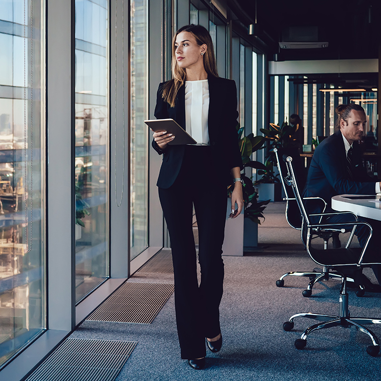 Serious female administrative manager in formal suit walking in office with digital tablet for checking office working process, confident woman business owner looking at window passing with touchpad