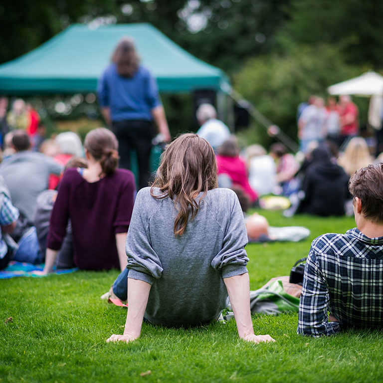 Friends sitting on the grass, enjoying an outdoors music, culture, community event, festival.