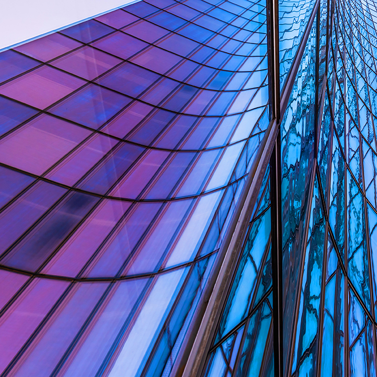 Curved modern glass building against sky with reflections.