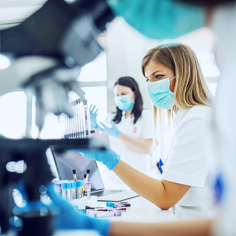 Small group of female laboratory assistants checking blood, using microscope and doing test for bacteria.