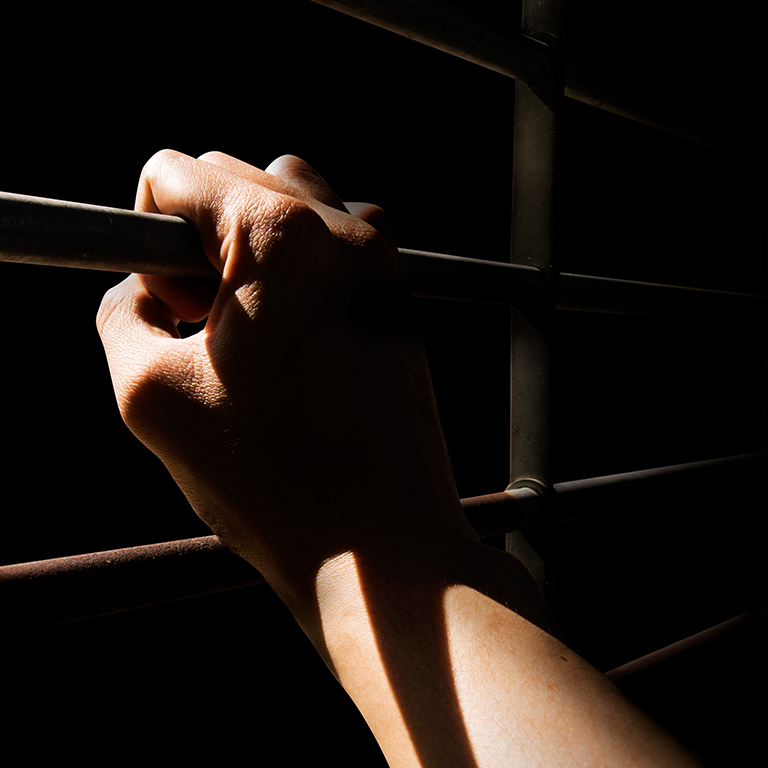 Close up a man's hand holding the cage door in dark room.