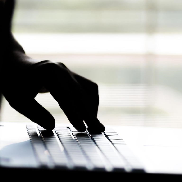 Hand reaching out through laptop computer and signifying a cyber crime in internet theft while using online
