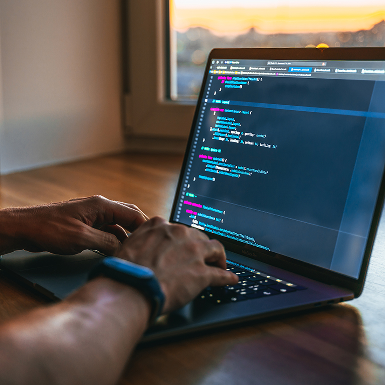 Man coding on a laptop at home or a cafe overlooking  a window in sunset