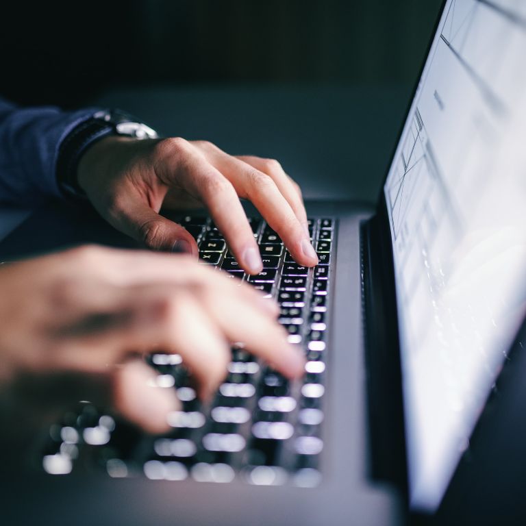 Hands typing on a laptop in a dimly lit room