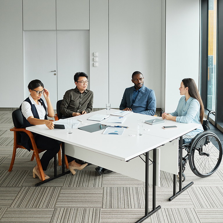 Vertical wide angle view at diverse business team discussing project at meeting table with focus on young woman in wheelchair sharing ideas