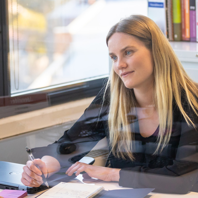 One person sat at a desk listening to someone and taking notes in a notebook