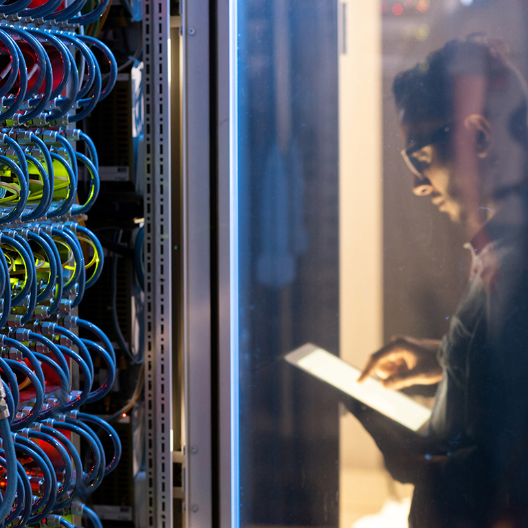 IT engineer testing new supercomputer while using digital tablet app, focus on open supercomputer cabinet with wires and cables