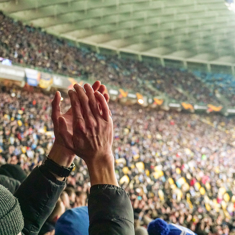 Large crowd of football fans clapping hands, supporting their team. Crowd of sports fans watching game at stadium