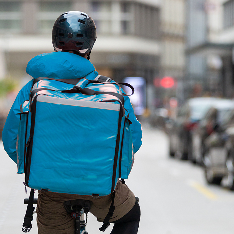 Unrecognizable courier on bicycle delivering food in city. 