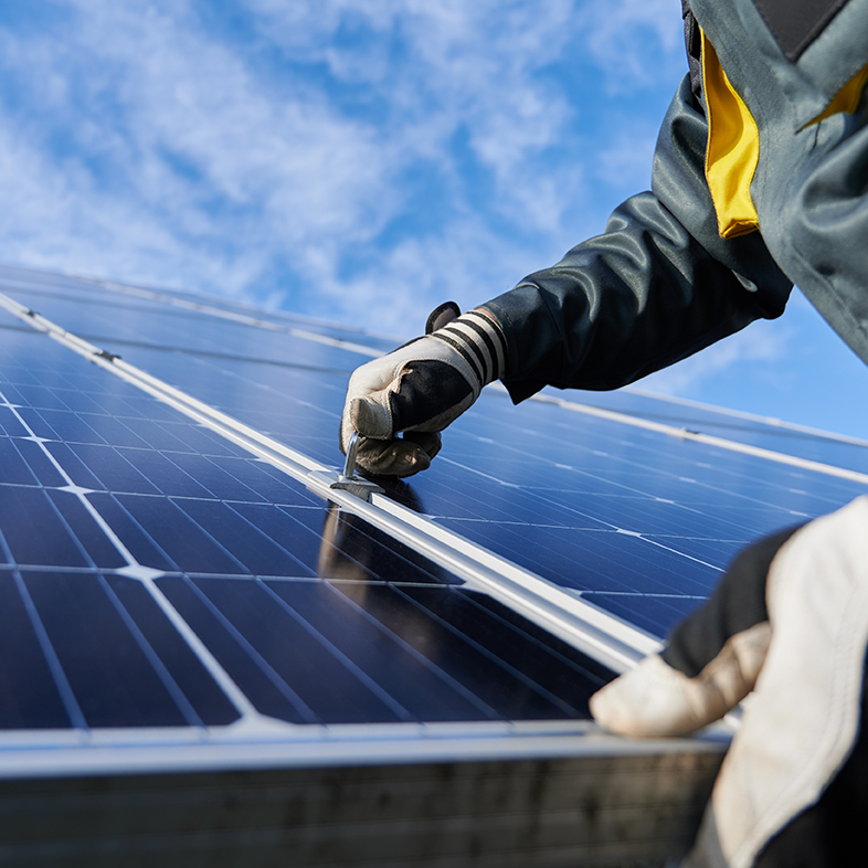 Close up of man technician in work gloves installing stand-alone photovoltaic solar panel system under beautiful blue sky with clouds. Concept of alternative energy and power sustainable resources.