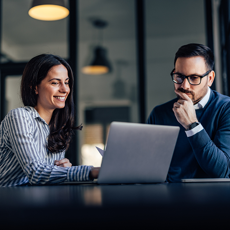 Brunette woman and man with glasses, working together with laptop while sitting in the meeting room.