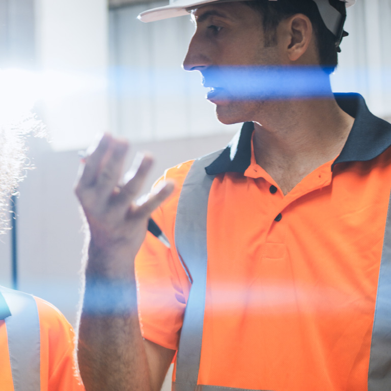 Worker in hi vis orange t-shirt talking seriously with a colleague in a warehouse