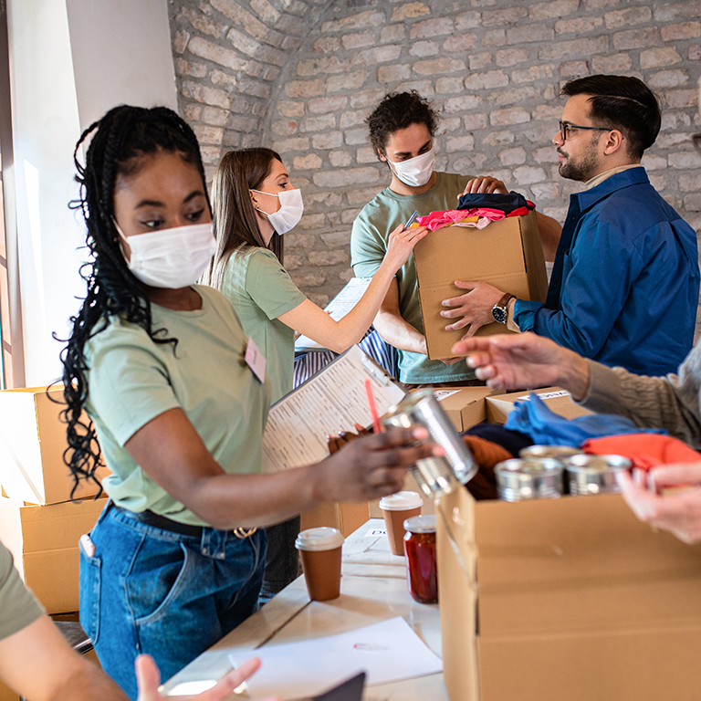 Group of volunteers with face mask working in community charity donation center.