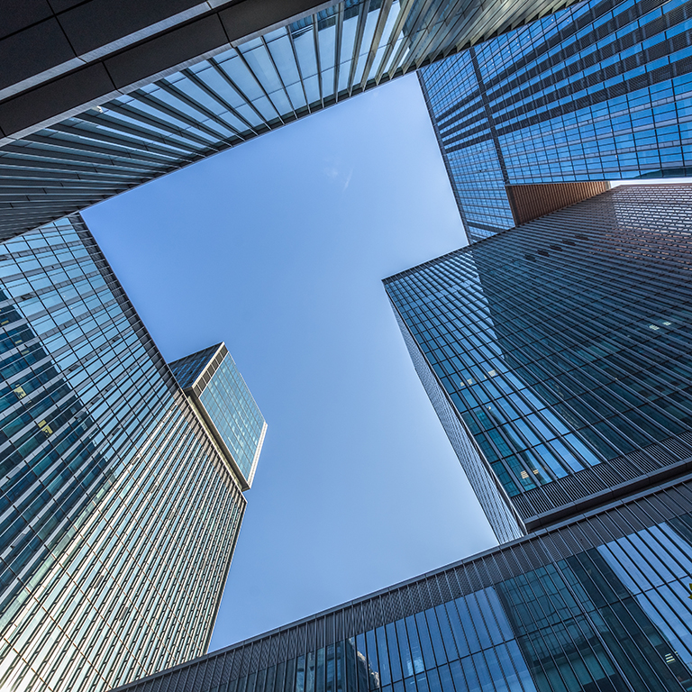 Bottom view of modern skyscrapers in business district against blue sky
