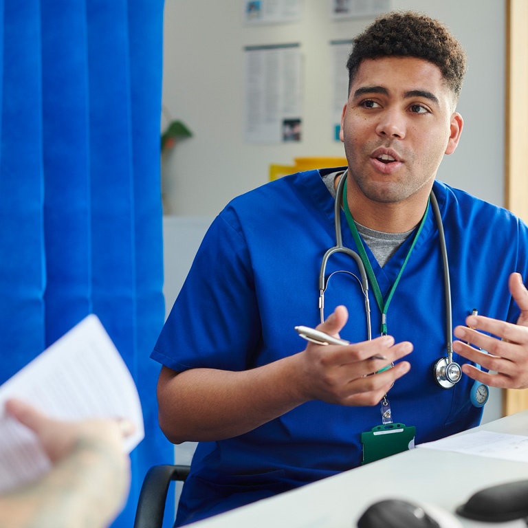 Healthcare worker in blue scrubs in consultation room speaking with a patient