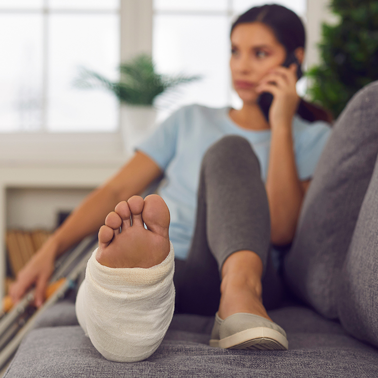 Young woman with a broken leg siting on a couch with crutches by her side.