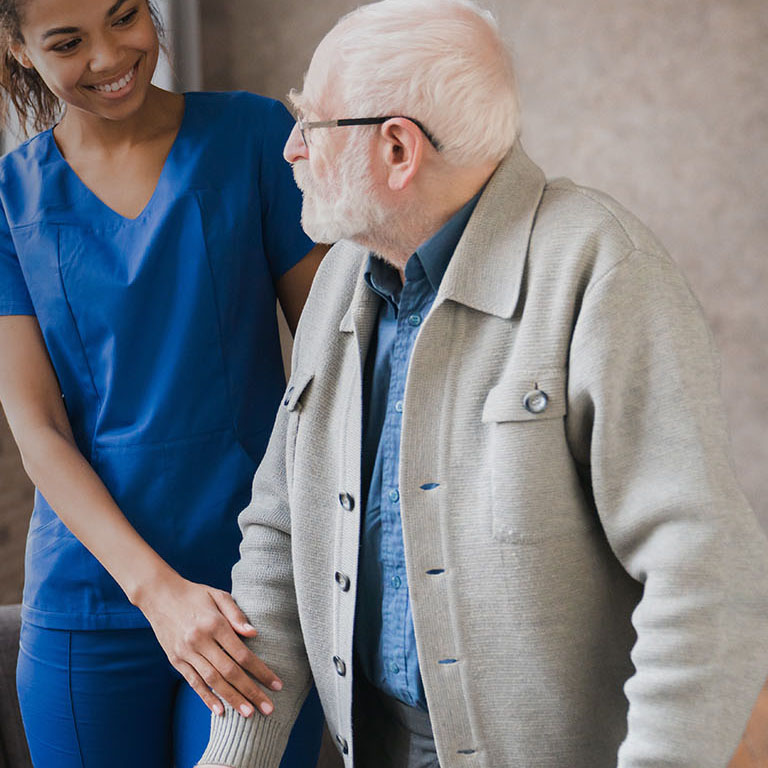 Portrait of an african young nurse helping old elderly disable man grandfather to walk using walker equipment in the bedroom. Senior patient of nursing home moving with walking frame and nurse support