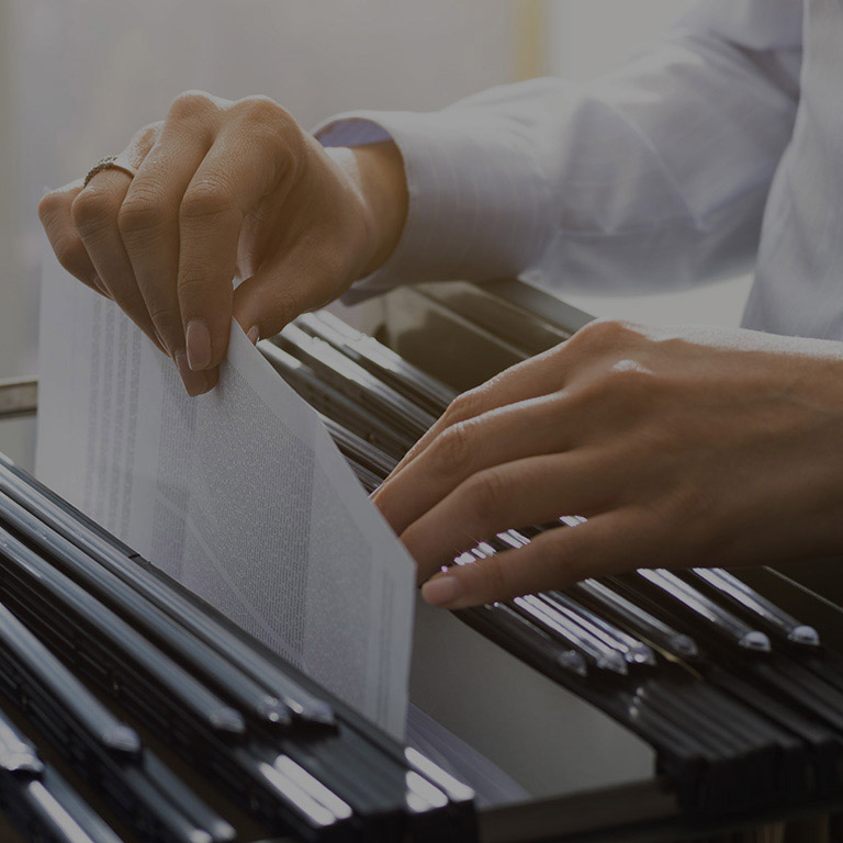 Professional female office clerk searching files and paperwork in the filing cabinet