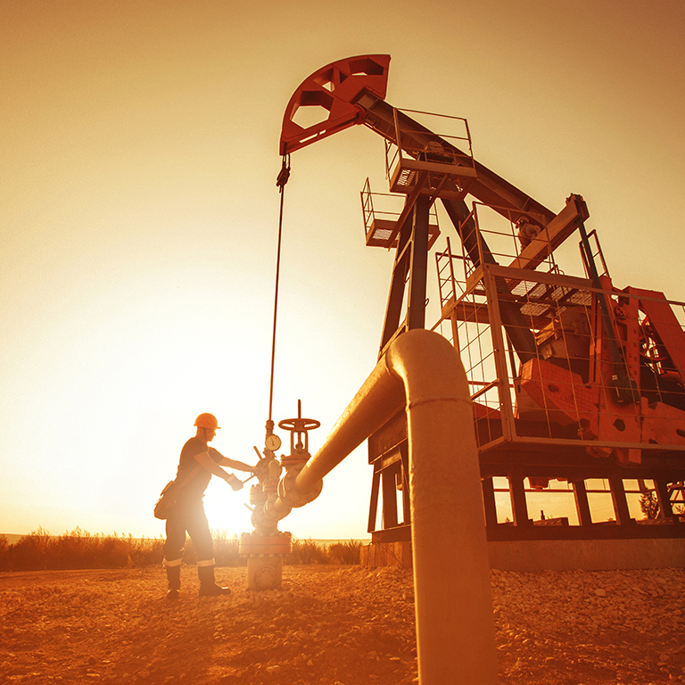 Oil worker is checking the pump near oil derrick on the sunset background.