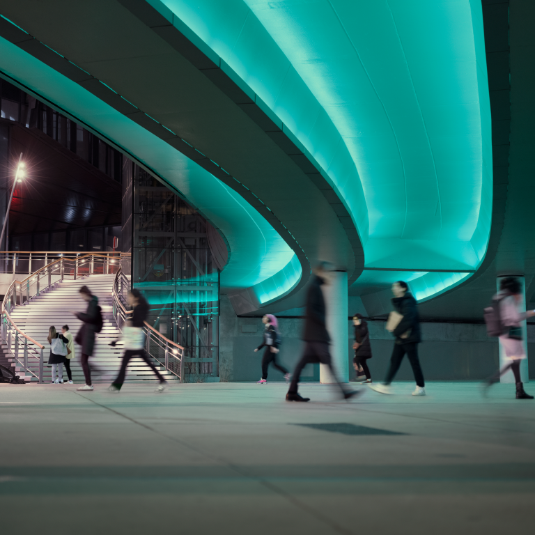 People walking under a lighted overpass in the city