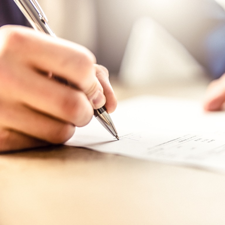 Person writes on paper in an indoor setting with sunlight