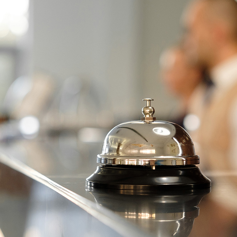 Modern luxury Hotel Reception Counter desk with Bell. Service Bell locating at reception. Silver Call Bell on table, Receptionists and customer on background. Сheck in hotel. Concept.