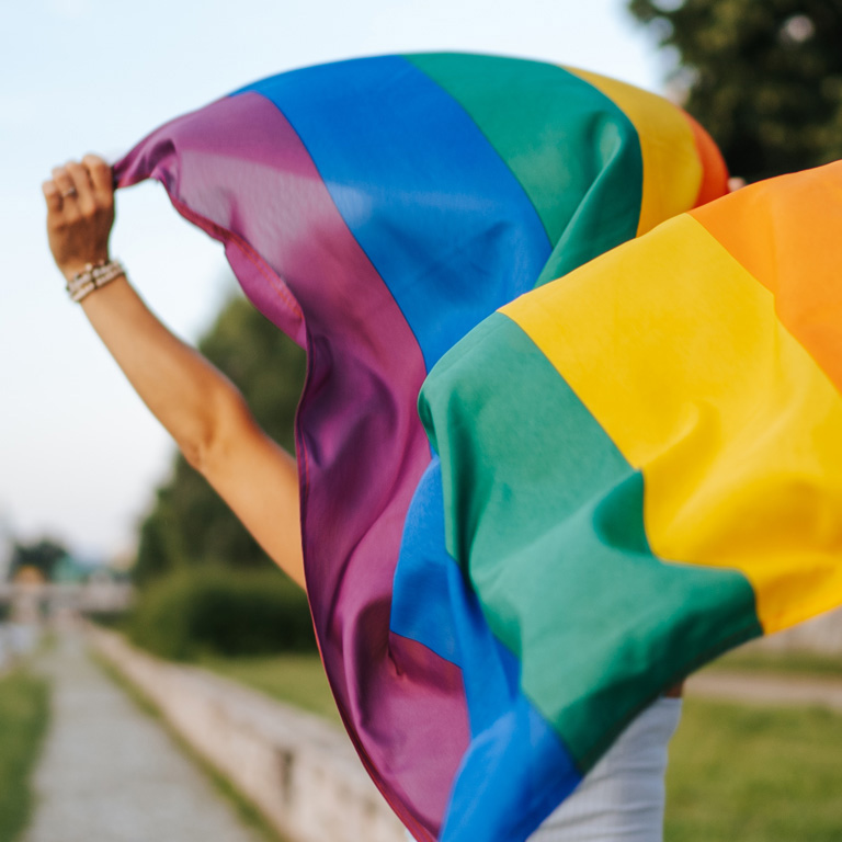 Young lesbian woman with rainbow flag running on city quay