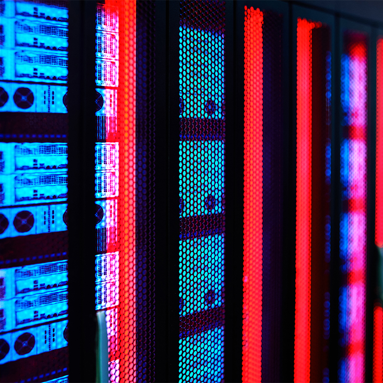 Several server racks are located in a data center. The racks display bright lights in blue and red. The scene shows the modern setup of technology equipment.
