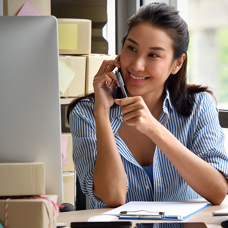 Young Asian woman entrepreneur/ Business owner using a smartphone and working with computer at home