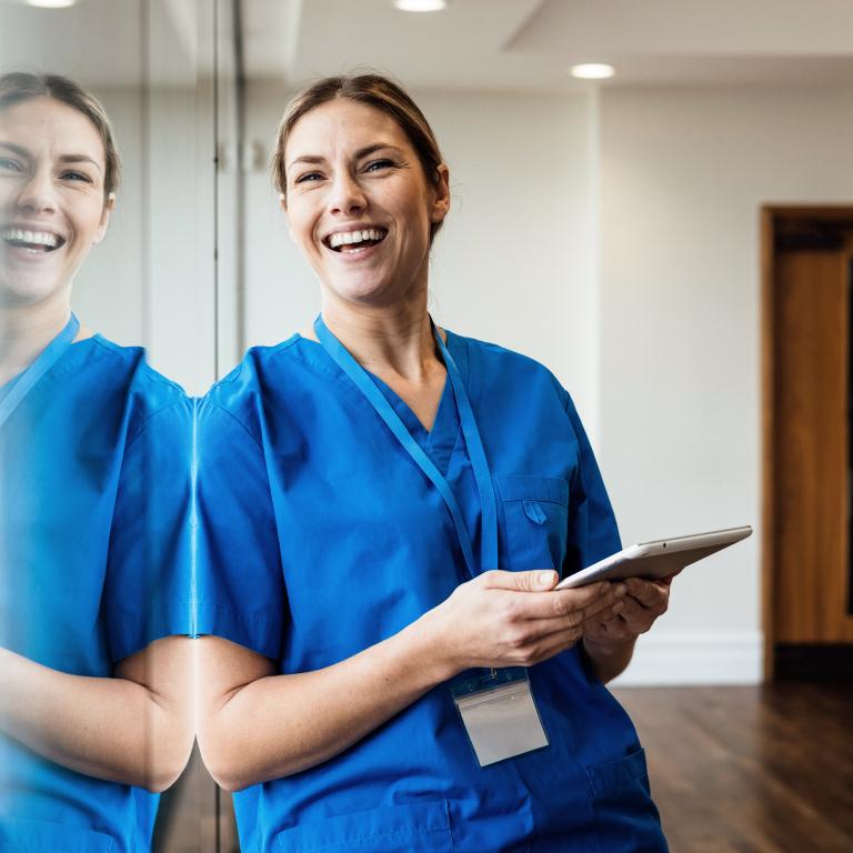 Smiling healthcare worker in blue uniform holds tablet