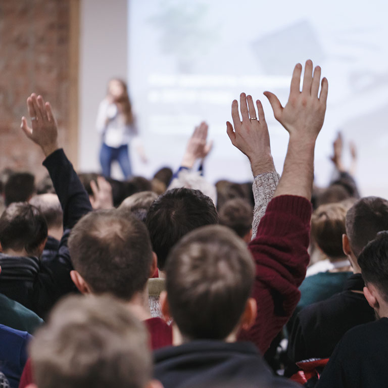 Adult students at large conference hall listen to woman speaker 