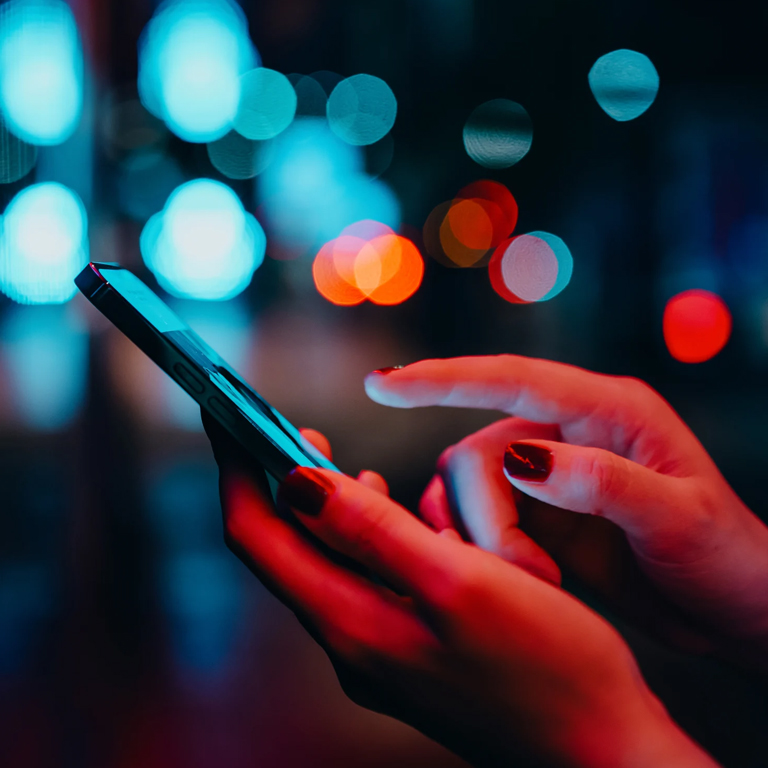 Hands texting on phone with lights on the background