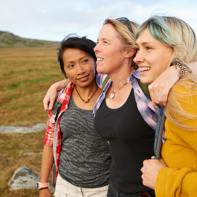 A group of happy and positive female hiking friends huddle together on a rocky moorland in an idyllic rural countryside.