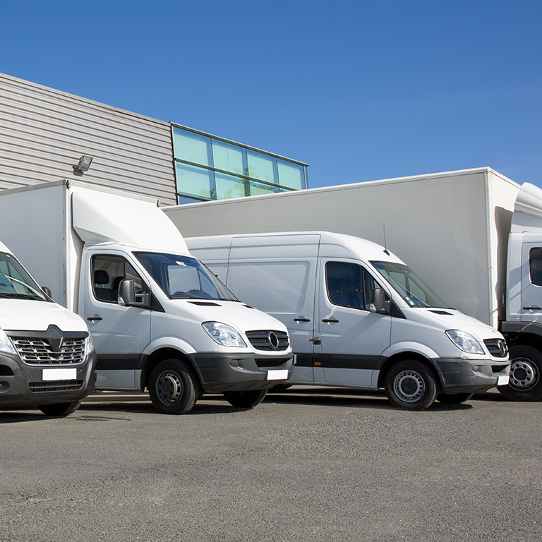 Transportation fleet of cargo trucks and courier service vans parked in front of warehouse/depot.