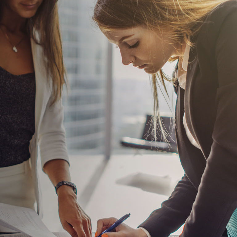 Two women signing a contract standing in modern appartment.