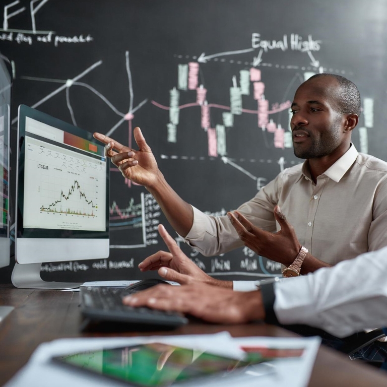 Two diverse colleagues traders discussing ideas while sitting in the office in front of multiple computer screens