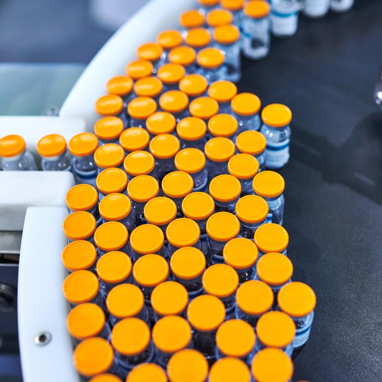 Vials with orange caps on conveyor belt in warehouse setting