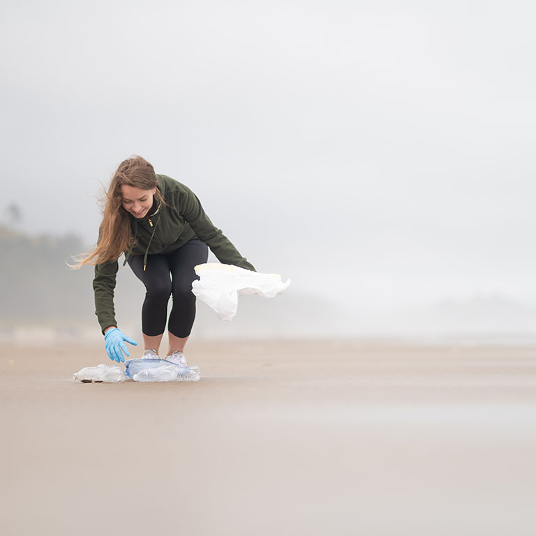 A volunteer collects empty plastic bottles and other garbage on the ocean shore. Environmental pollution, environmental and social problems. There is an empty space for insertion.