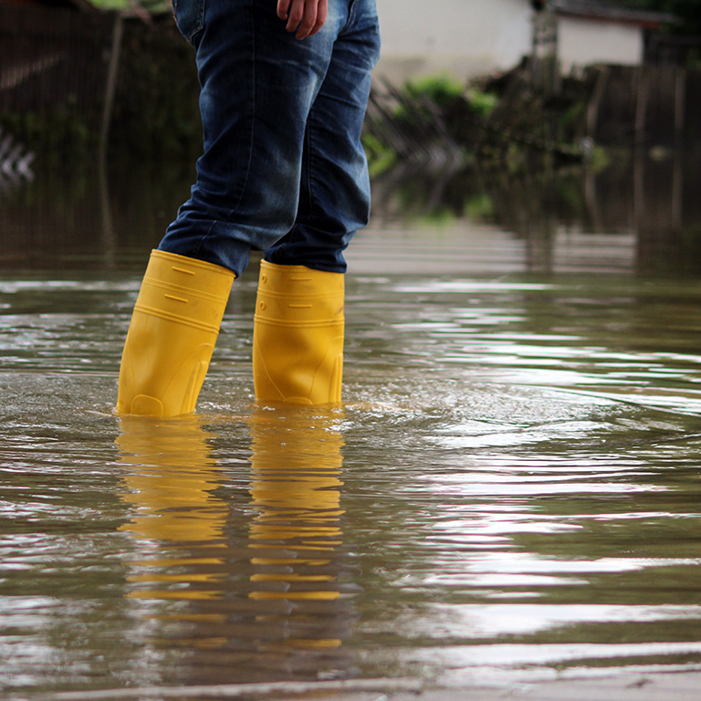 Close up of a person wearing wellies trying to walk through a flood.