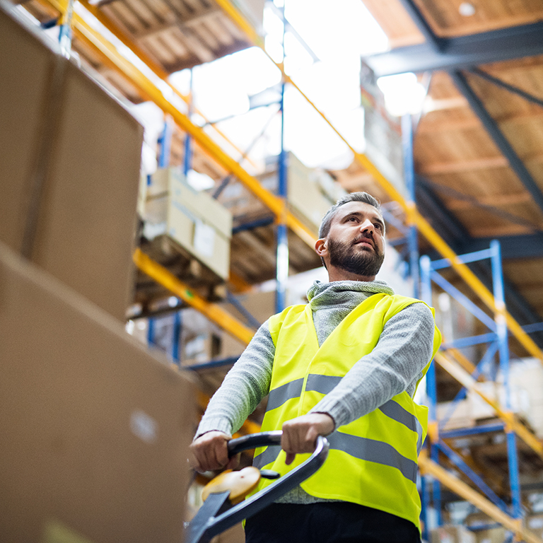 Young male warehouse worker pulling a pallet truck with boxes.