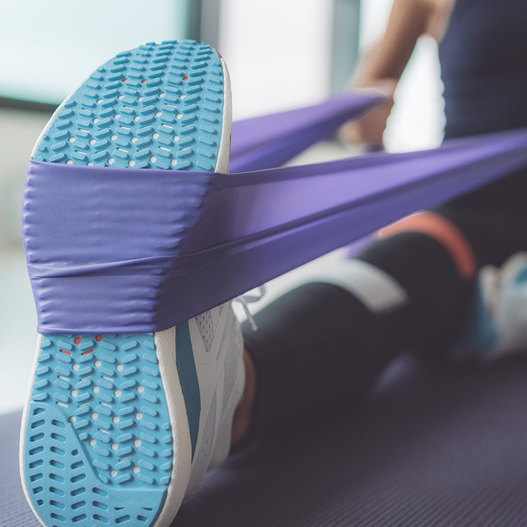 Resistance band exercise at home. Woman doing pilates workout using elastic strap pulling with arms for shoulder training on yoga mat indoors.