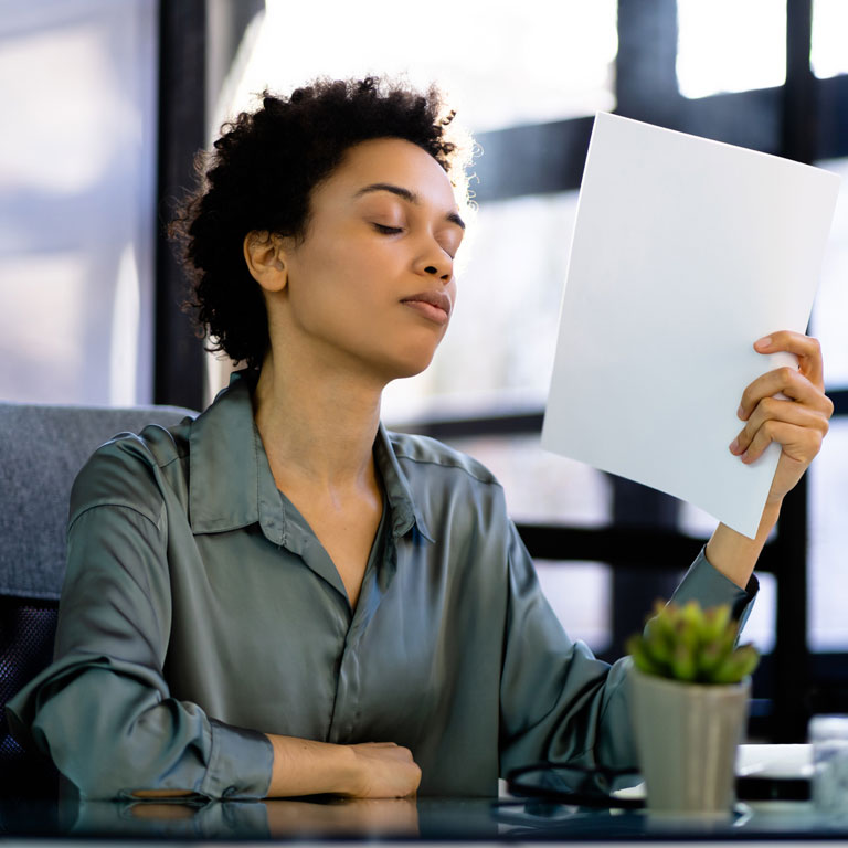 Woman fanning herself with paper extreme heat in workplace