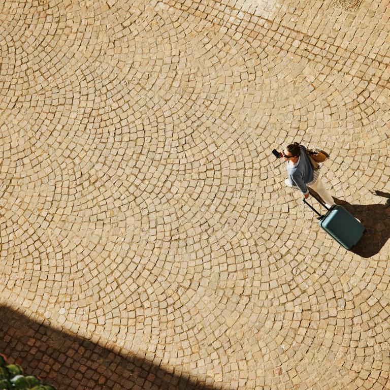 Woman walking with suitcase on cobblestone path in sunlight