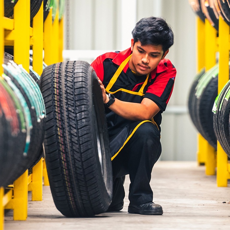 Worker lifts tire in tire storage area during daylight hours