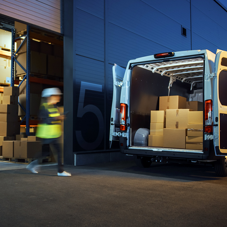 Outside of logistics distributions warehouse diverse team of workers loading delivery truck with cardboard boxes. Online orders, purchases, e-commerce goods, supply chain. Blur motion shot.