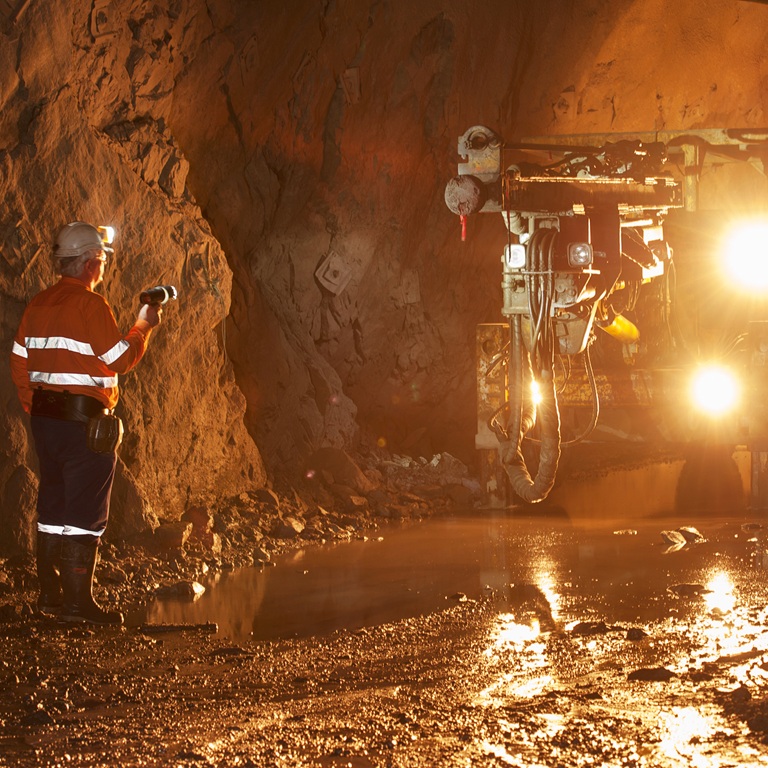 Workers operate mining equipment in dark tunnel