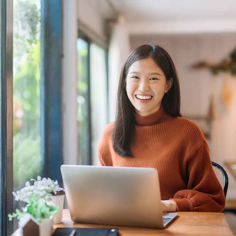 Happy young Asian girl working at a coffee shop with a laptop 